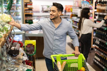 Middle Eastern Male Doing Grocery Shopping Buying Vegetables In Modern Supermarket