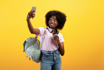 Happy african american lady taking selfie on smartphone, wearing backpack and holding coffee to go