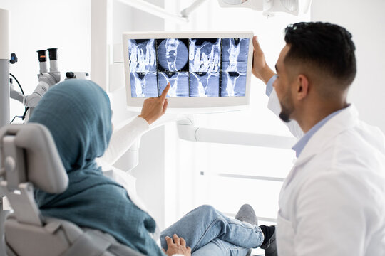Male Dentist Showing Teeth Xray Picture On Digital Monitor To Muslim Woman
