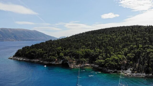 Tourists Swimming In Emerald Crystal Water Of Foki Beach In Kefalonia Island, Greece With Densely Forested Hill. wide aerial