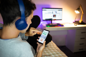 Young man shopping online at home and paying via PIX.  PIX is a new electronic payment system in Brazil.