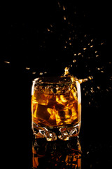 glass of whiskey with ice and splash on a black background