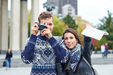 Happy love couple of tourists taking photo on excursion or city tour. Travel together with a map and retro camera