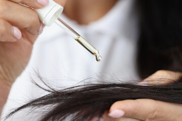 Girl hold dropper with castor extract oil near hair and apply one drop