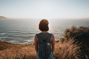 Back image of a young backpack traveler hiker during an stunning sunset coastline scenario, hipster...