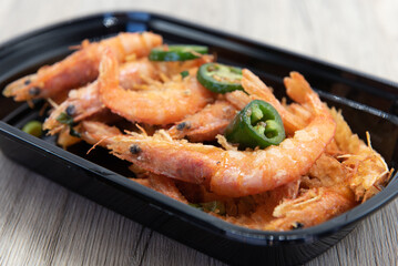 Jalapeno peppers chopped over the pepper seasoned shrimp with heads still on for a delicious seafood dish.
