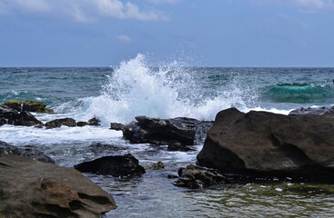 Obraz premium View from the rocky coast to the sea, splashes from the waves, large stones in the foreground