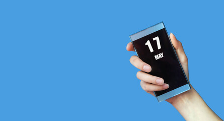 may 17. 17th day of the month, calendar date.Woman's hand holds mobile phone with blank screen on...