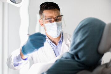 Fototapeta na wymiar Young Arab Stomatologist Making Check Up To Islamic Woman In Modern Clinic