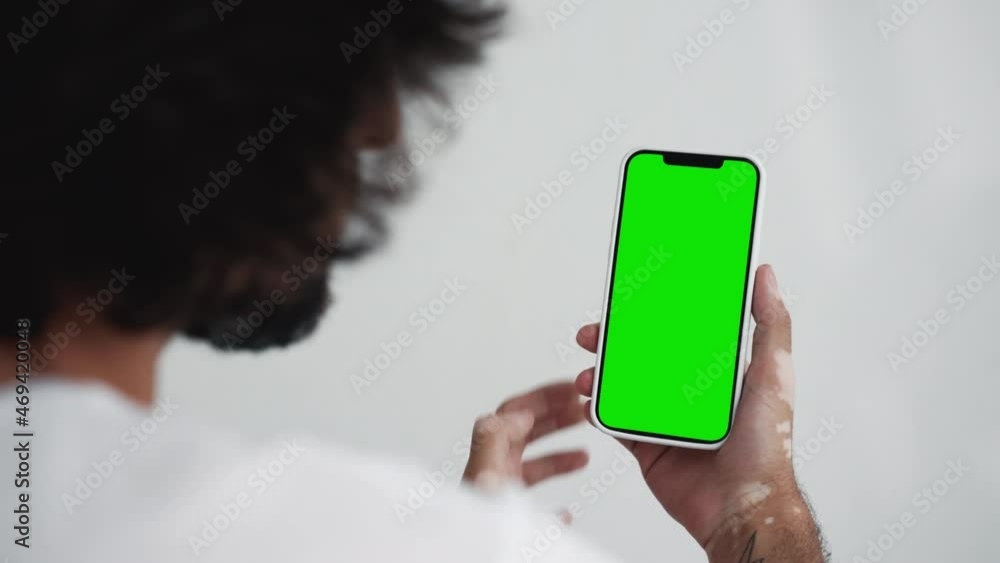 Poster back view young man look phone with green screen and swipe touch close-up. guy hold use click gestur