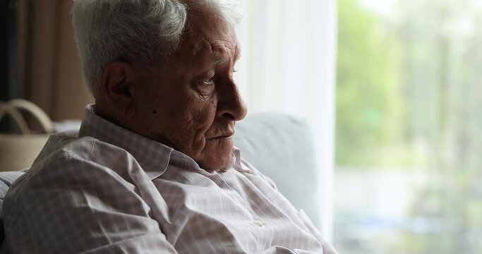 Close up profile wrinkled face of hoary senior adult man rest indoors stare forward with sad look lost in pessimistic thoughts. Lonely older male pensioner having life problems need psychological help