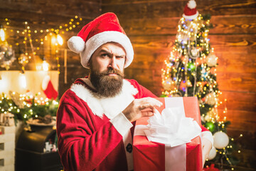 Fototapeta na wymiar Hipster in red Santa hat holding present. Styling Santa man with a long beard posing on the Christmas wooden background.