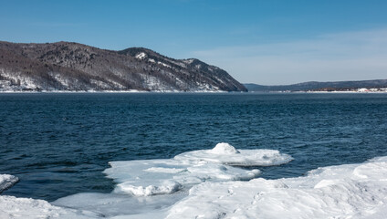 Winter ice-free river Angara. Blue water and white icy shores. A mountain range against an azure sky. A sunny day. Siberia