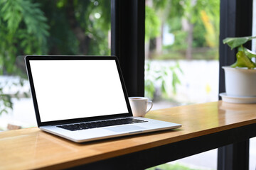 Computer laptop with lank display and cup of coffee on wooden table.