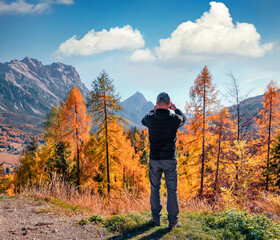 Tourist takes picture on smaptphone outskirts of Cortina d'Ampezzo town. Amazing autumn view of Dolomite Alps. Stunning outdoor scene of Italy, Europe. Traveling concept background..