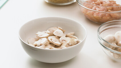 Pasta with chicken and mushrooms recipe. Raw chopped mushrooms and raw chopped chicken fillet close up in bowls, white background, copy space