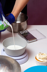 Milk is poured into a bowl, next to there is a scale for measuring grams and there is a ready-made cupcake. Selective focus.