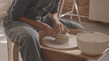 Cropped woman in casualwear working with pottery wheel in cozy workshop
