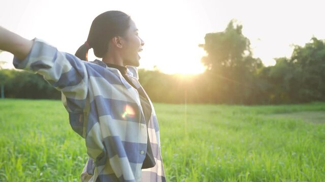 Young asian girl feeling happy and fresh standing on the green grass field enjoy warm morning light, good way to start a day, golden hour with sun light on the background, nature happiness sustainable