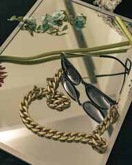 jewelry on a mirror with glasses and a flower