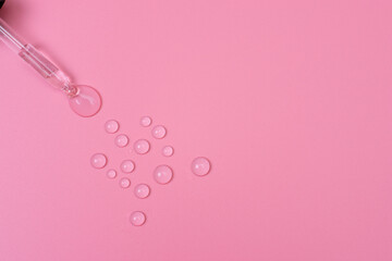 Drops of transparent liquid are squeezed out of a pipette on a pink background