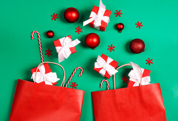 Two red paper shopping bags with Christmas decorations and gift on green background with copy space for text.