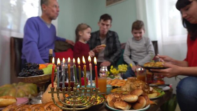 Lighting the Menorah lights. Menorah candles. Festive Hanukkah dinner at home with family. Traditional kosher Jewish food on the table - sufganiyot, latkes, cottage cheese and cheese meals