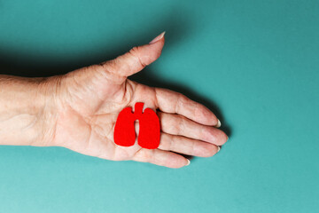 A senior woman shows in her palm, a silhouette of sick red lungs cut out of felt. Close up. Flay...
