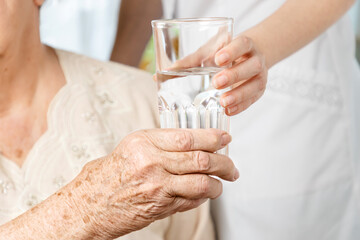 International Day of Older Persons. A nurse gives a glass of water to an elderly woman. Close up of hands. Care for the elderly in nursing homes