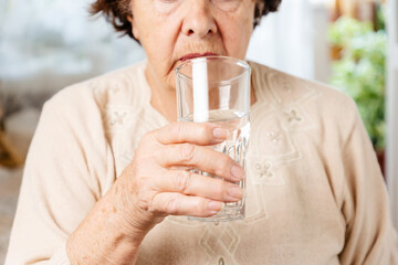 Senior woman holds a glass of water. Taking medications for pain. Close up. The concept of caring for the elderly