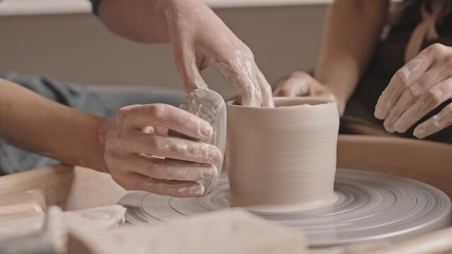 Slowmo close-up of unrecognizable female hands shaping pot out of clay working on pottery wheel in workshop