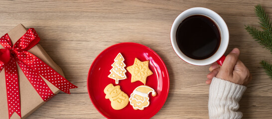 Merry Christmas with woman hand holding coffee cup and homemade cookie on table. Xmas eve, party, holiday and happy New Year concept
