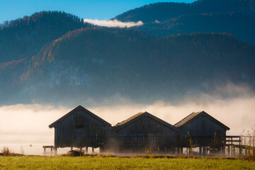 Berge im Nebel und Bootshäuser in Schlehdorf am Kochelsee