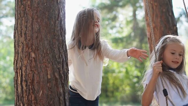 Cute kids ride a swing in the park. Summer.