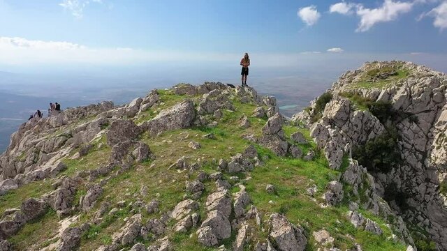 Drone shot of a young, fit and handsome man with tattoos, beard and long hair standing topless on top of Zaghouan in Tunisia. Flying backwards to reveal the epic mountainside and landscape around.