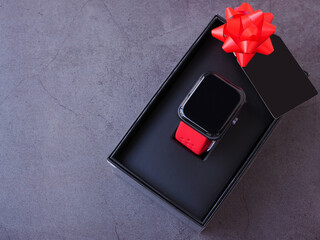 Smartwatch in the black gift box tied with a red bow and black greeting cards on dark grey...