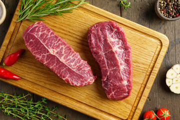 Fresh two raw top blade beef steak on wood board with condiment and herbs