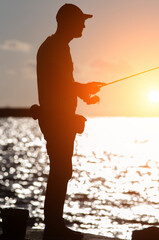 A fisherman wearing a cap takes part in a sea fishing competition at sunset.