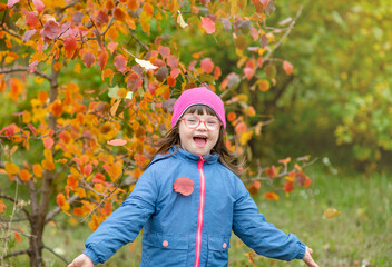 Joyful girl with Downs syndrome throwing autumn leaves at autumn park