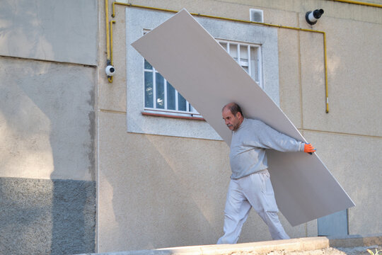Senior worker carrying plasterboard sheets.