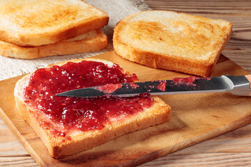 Toast with red jam on wooden board. Selective focus.