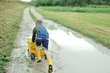 Little boy plays with toy cars in a puddle on a dirt road.
