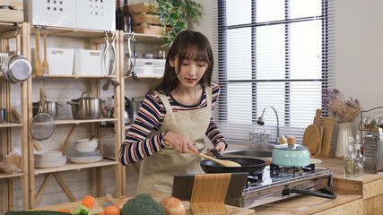 asian girl under quarantine practicing cooking at home, learning via the internet. young lady pan-frying food and looking at pad in the kitchen. modern technology, real moments