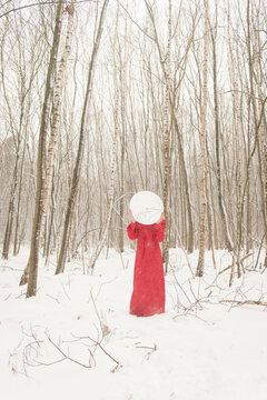 Abstract art portrait of woman in red dress standing in snow in winter forest landscape holding mirror