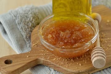 Homemade lip scrub made out of brown sugar, honey and olive oil in glass bowl on wooden chopping...
