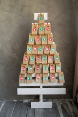 Handmade advent calendar presents in craft bags hanging on a wooden Christmas tree. Creative...