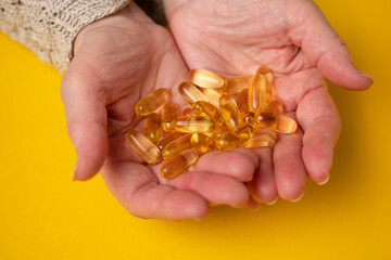 Fototapeta premium Elderly woman holds fish oil capsules in her hands. Omega 3 and old age.