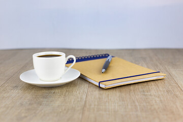 A cup of coffee, a craft notebook and a pen on a wooden table.