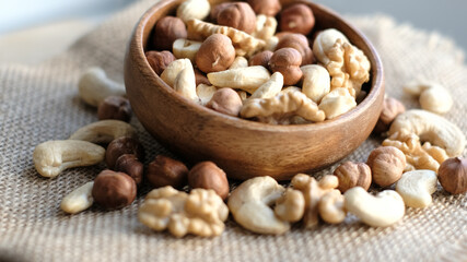 mixed nuts in a wooden cup against the background of fabric from burlap. Walnut, hazelnuts and cashews. Wood bowl with different tasty nuts