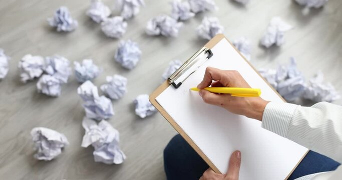 Woman writing business plan on paper among crumpled documents scattered on floor closeup 4k movie slow motion